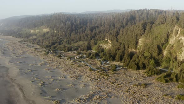 A slow panning drone shot of a campground near redwood trees and a beach and ocean waves.