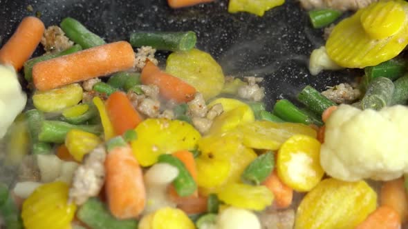 Close up view of steaming frying pan and mixed vegetables with frying minced