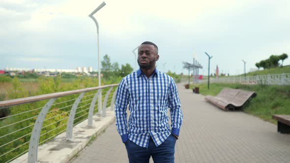 Young Afro American Man is Walking in City Park in Cloudy Summer Day