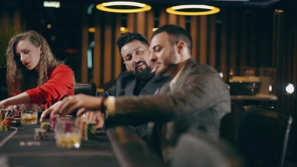 Two Bearded Men and Young Woman are Looking Intently at Their Poker Playing Cards Make Bets