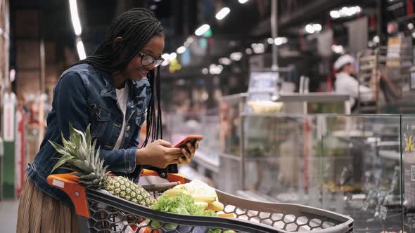 African Amercan Girl with Phone and Trolley in a Supermarket