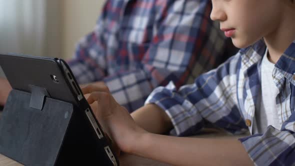 Boy Using Tablet, Surfing Internet, Playing Easy Games While Father Working