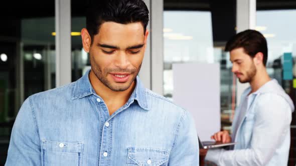 Portrait of male executive using mobile phone with his colleague in background