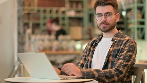 Young Man with Laptop Looking at Camera in Cafe 