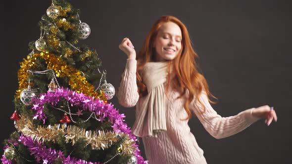 Portrait of Redhead Girl Smoothly Dancing Near Christmas Tree in Studio on Black Backgraund.