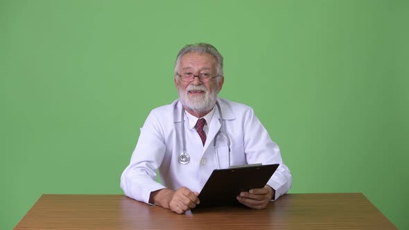 Handsome Senior Bearded Man Doctor Against Green Background