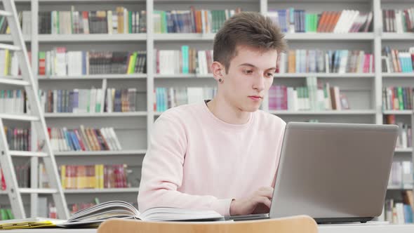 Young Male Student Working on His Laptop at College Library