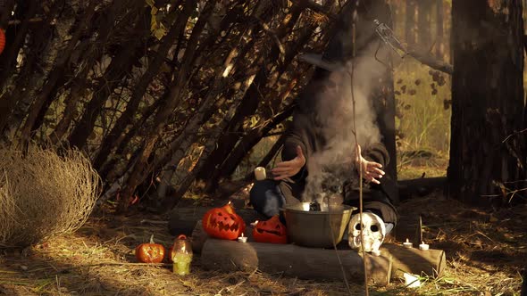 Young Witch with Sugar Skull Makeup Waves Hands Over Kettle with Smoke