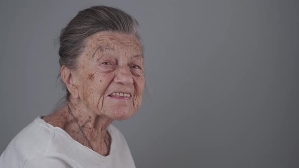Senior Woman 90 Years Old Smiles Laughs and Shows a Denture on a Gray Background