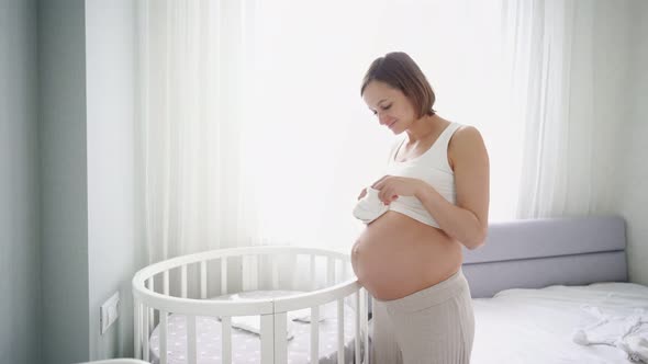 Young Pregnant Woman with Small Baby Shoes Sitting on Sofa at Home