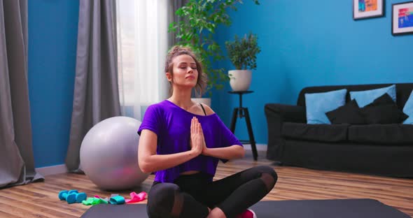 Portrait of Beautiful Young Woman Dressed in Fitness Clothes Meditates While Sitting in Lotus