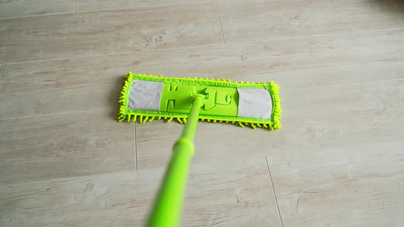 Green microfiber mop moving on the parquet floor to keep the house clean