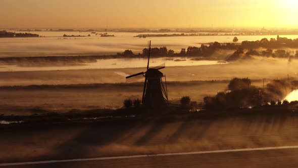 Low aerial shot of a dramatic silhouetted windmill and farm fields with a light fog clinging to the