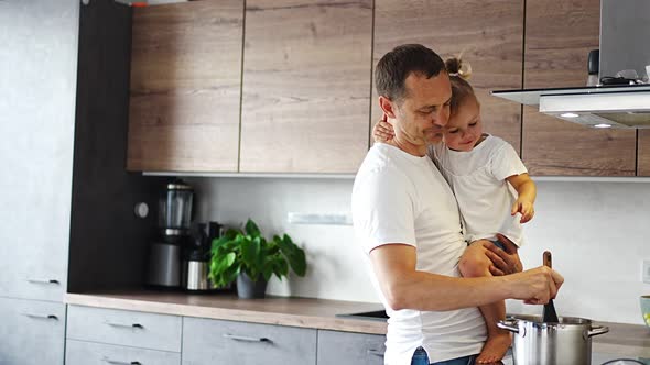 Father with His Daughter on His Hands Cooking Soup Together in Modern Home Kitchen