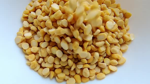 Static close up shot of raw moong dal grains falling on white plate