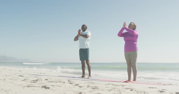 Senior african american couple practicing yoga on mats on sunny beach