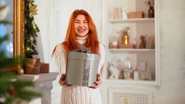 Beautiful Woman Smiles at Camera with New Year Gift in Hands Near Christmas Tree