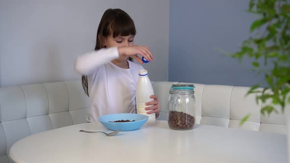 Little Girl Pours Milk to Chocolate Corn Balls Sitting at Table