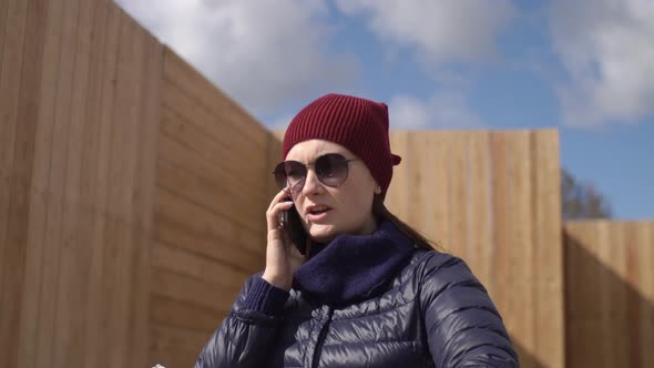 Woman in Red Hat Goes Down Street Talks on Phone Holds an Album Negotiates