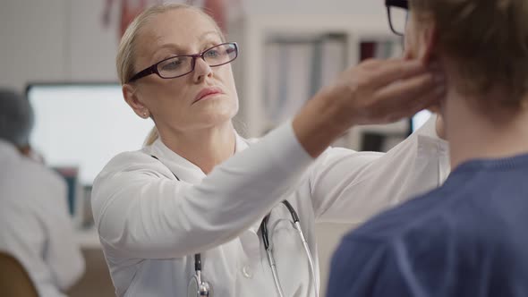 Senior Female Physician Checking Patient Throat and Neck in Hospital Office