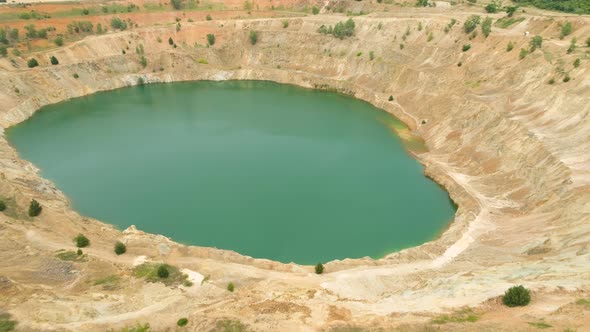 Unrecognizable Woman Sitting on the Edge of Abandoned Mine Pit Full of Water and Taking Photos