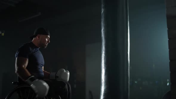 Portrait of a Disabled Man Fighter in Wheelchair Man Trains Punches on a Punching Bag Training in