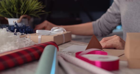 Woman writing postcard and wrapping a gift in living room