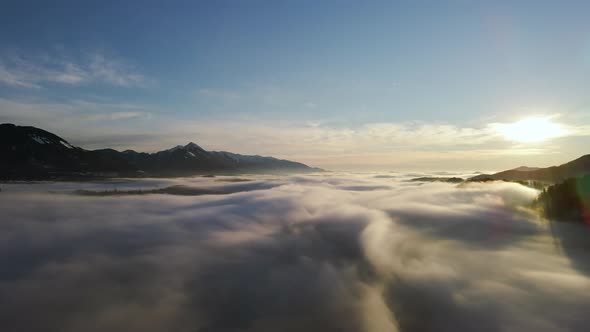 Drone shot  of an incredible landscape covered under the fog with surrounding mountains in the morni