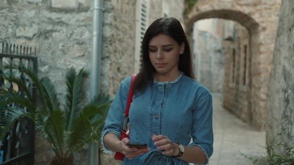 Pretty young woman tourist with brunette hair  in denim overalls walks and looking at map