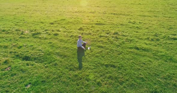 Low Orbital Flight Around Man on Green Grass with Notebook Pad at Yellow Rural Field