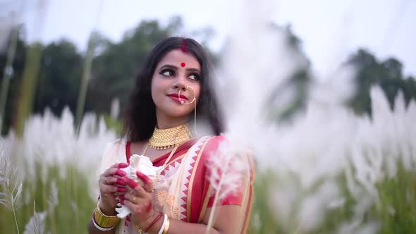 A romantic and thoughtful Indian married woman looks away holding a conch shell or shankha in a fiel