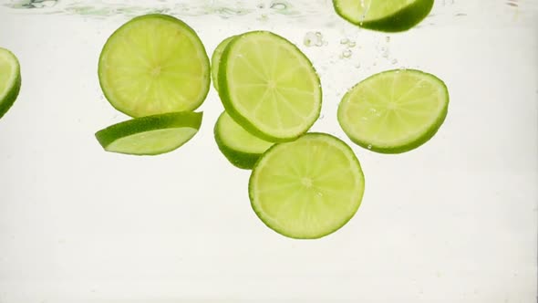 Cut Into Slices Round Pieces of Lime Fall Into the Water, Slow Motion Close-up