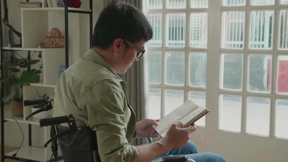 Asian Man Sitting In A Wheelchair Reading Book Near Door In The House