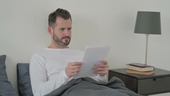 Man Reading Documents in Bed