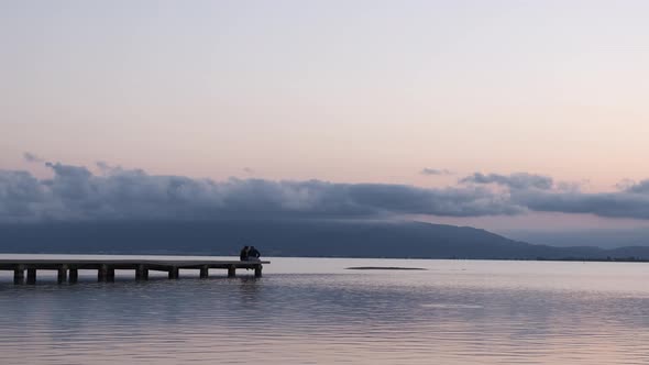 Unrecognizable couple relaxing on quay near sea in evening under sundown sky in summer