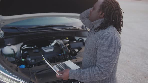 Young Upset African American Black Man Repairing the Car While Using Laptop