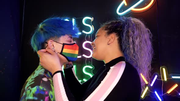 Cheerful lesbian girlfriends kissing against neon inscriptions