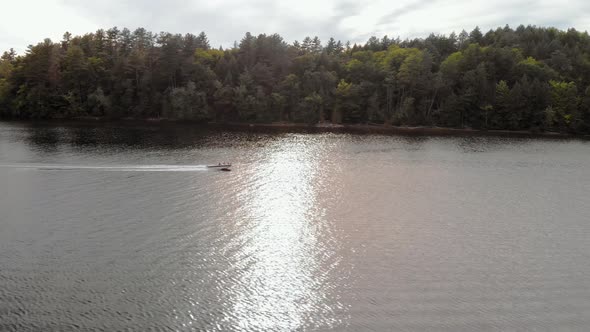 Pan right tracking speedboat moving across blue lake with forest of trees