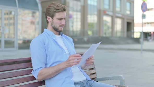 Young Man Reading Documents While Sitting on Bench Outdoor