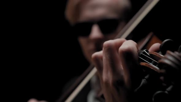 Young Caucasian Male in Black Suit and Glasses Plays Violin on Dark Background