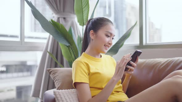 Young Asian woman using smart phone on sofa happy and smile.