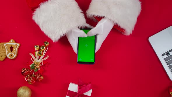 Top View Santa Hands Uses Smartphone with Green Screen Chroma Key By Red New Year Decorated Table