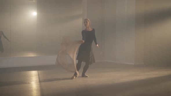 Wide Shot Graceful Ballerina Jumping in Arabesque Ballet Position in Backlit Fog Reflecting in