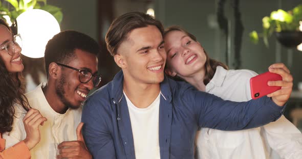 Young Cheerful Colleagues Smiling and Looking at Smartphone Screen While Taking Picture. Happy