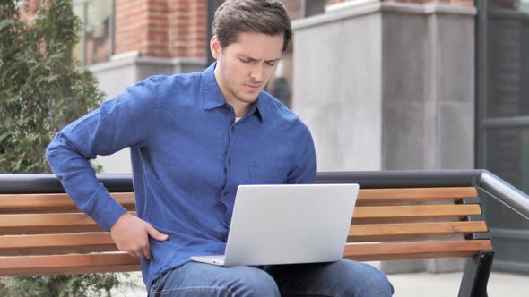 Sitting Outdoor Young Man with Back Pain Working on Laptop