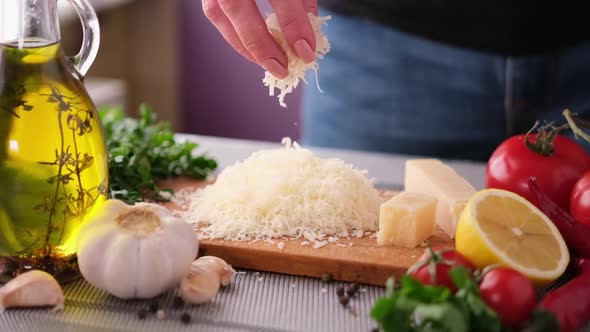 Woman Pours Grated Parmesan Cheese on Wooden Board at Domestic Kitchen