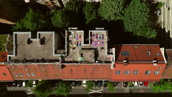 Aerial view of a group of people doing yoga on a rooftop at the city in summer.