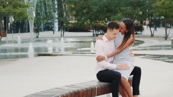 Mixed-race Man and Woman in Love Sitting on the Bench in Park, Hugging and Talking
