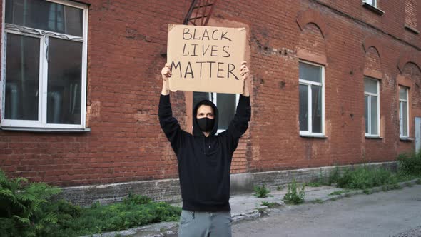 Man in Mask Stands with Cardboard Poster in Hands  BLACK LIVES MATTER