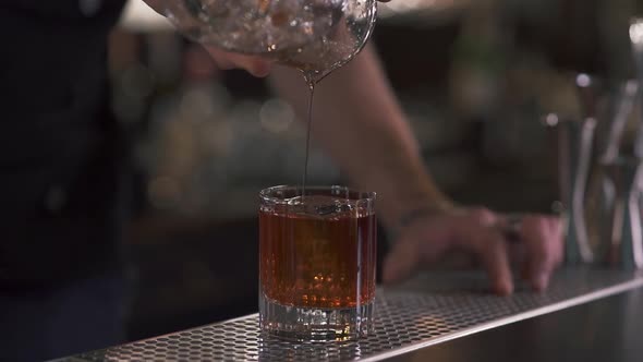 Male Hand Bartender Pours Liquid in the Glass with Big Ice Cube in It